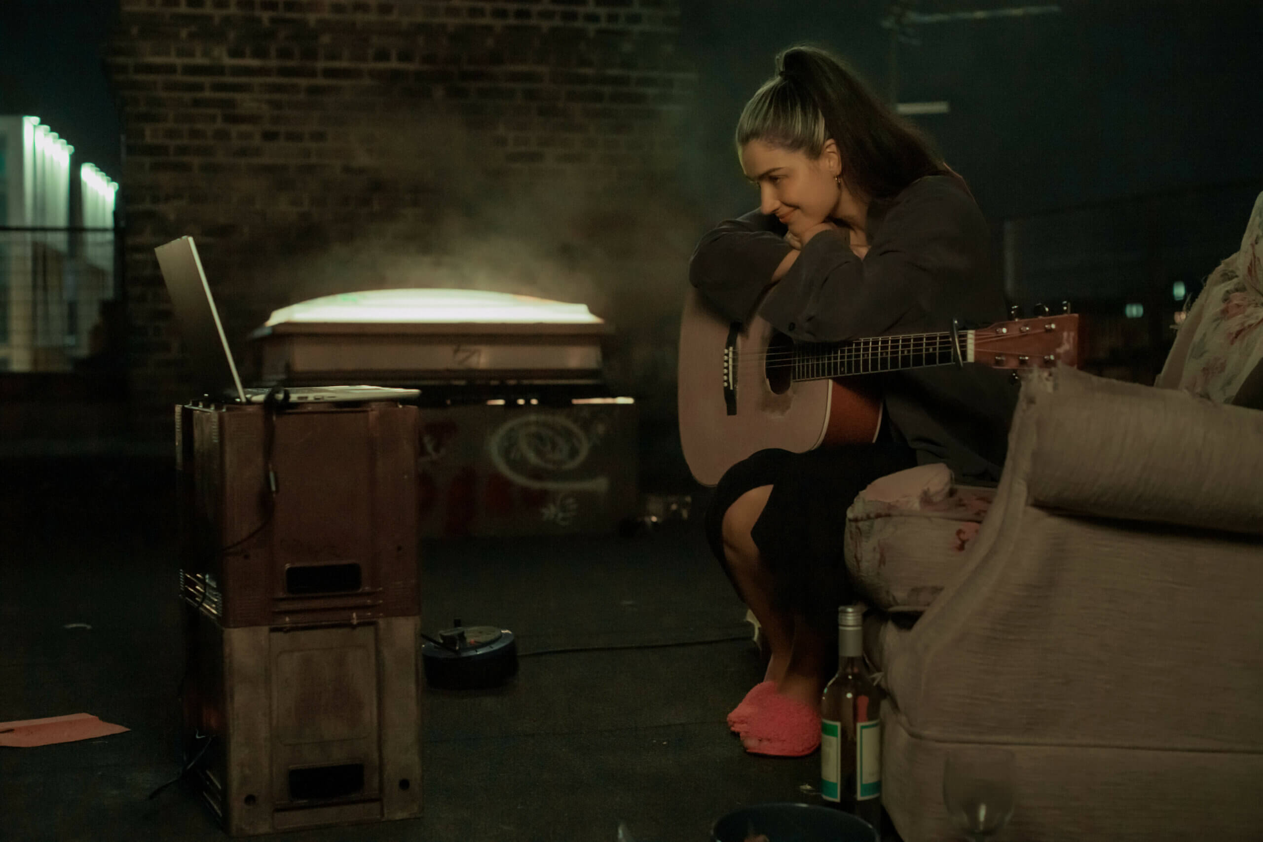 Eve Hewson sitting with a guitar listening to music inside.