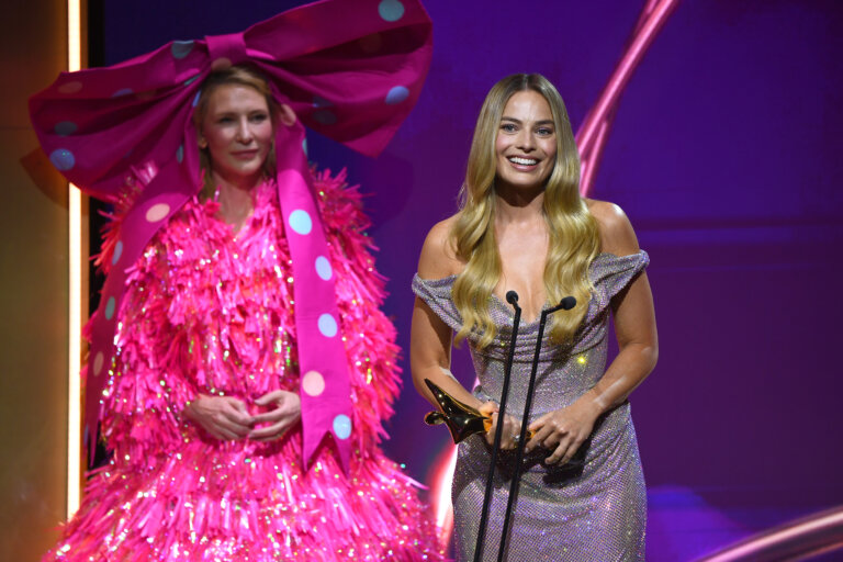 Margot Robbie and Cate Blanchett in a Barbie outfit posing with an award.