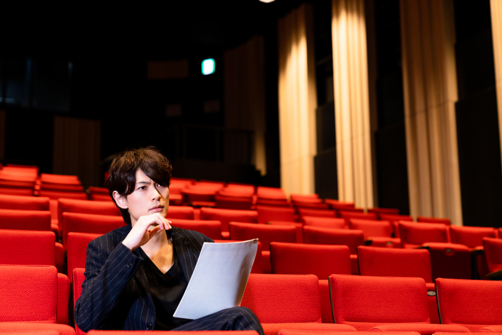 A director looking at the script in the theater stands while watching his play rehearsal.