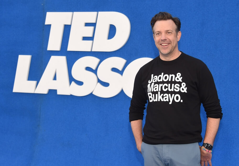Jason Sudeikis smiling in front of the Ted Lasso logo.