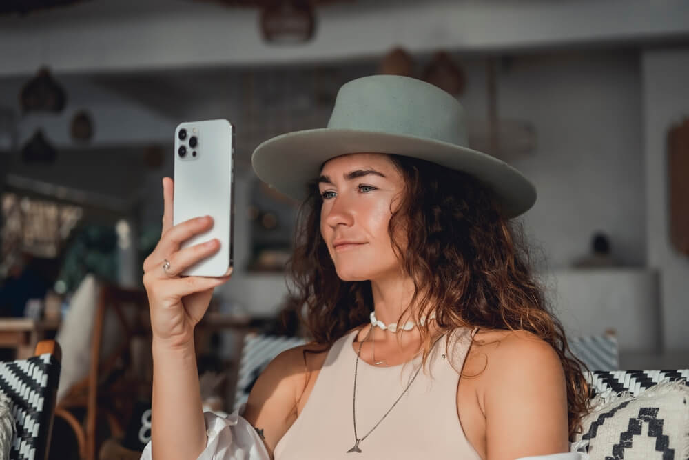Young woman with curly hair in a hat scrolling on her iPhone.