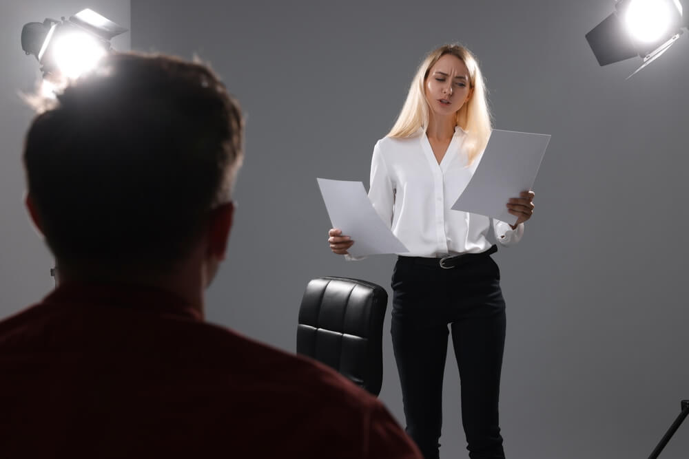 A woman in a white shirt auditioning in front of a casting director.